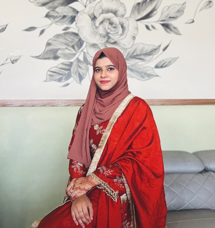A woman in a red hijab sits on a couch, representing a digital marketing freelancer in Kerala, focused and engaged.